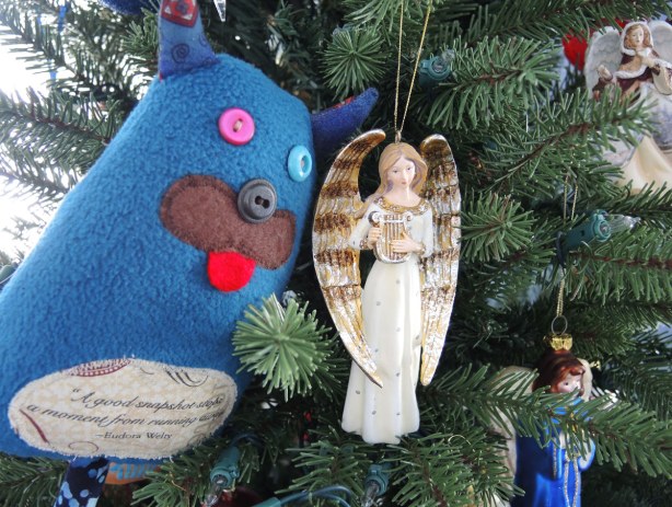 Edgar is sitting in a Christmas tree swooning over an angel Christmas ornament.  The angel is playing a lyre.