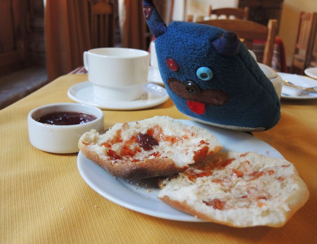 Edgar is leaning over, and looking at, a plate with a bun that has been cut in half.  There is strawberry jam spread on the bun.  It is on a white plate.  A small bowl of strawberry jam is beside him. 