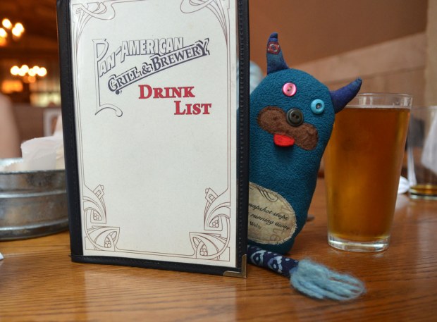 Edgar is peeking out from behind a drinks menu at a bar.  He is on the table along with a full glass of beer. 