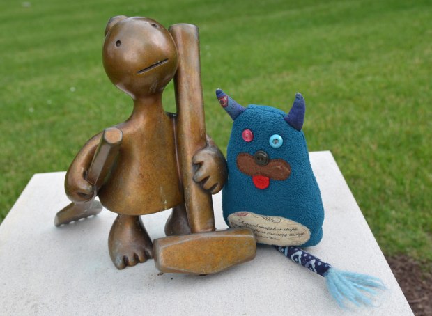 Edgar is standing beside a llittle bronze figure who is holding a hammer in her hand.