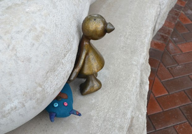 Edgar, the little blue monster, is wedged between two large pieces of limestone, a little bronze figure is trying to lift the upper rock so Edgar can get out.