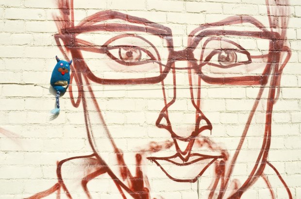 edgar is standing beside the ear of a face painted on a wall by street artis anser - a man's face, wearing glasses